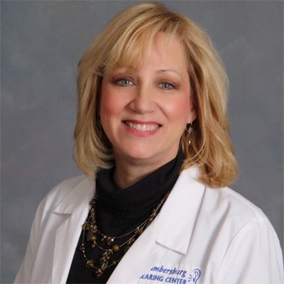 Victoria middle aged, blonde female wearing a white professional jacket sitting in front of a gray background